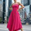 Stylish woman wearing a pink smocked midi dress standing confidently on a modern city street with skyscrapers in the background