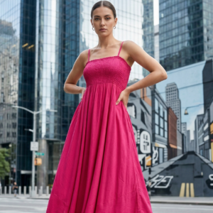 Stylish woman wearing a pink smocked midi dress standing confidently on a modern city street with skyscrapers in the background